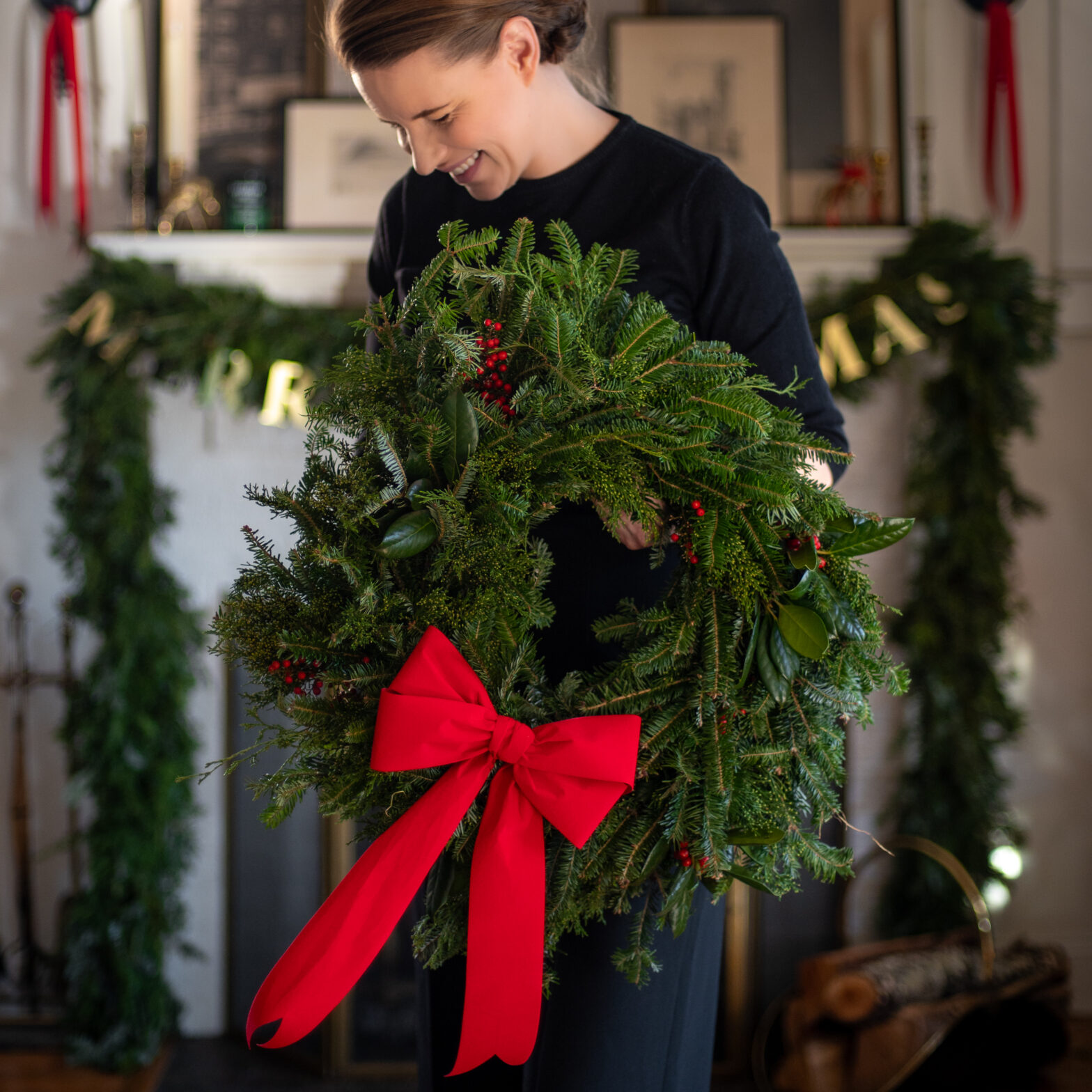 Woman holding a fresh evergreen wreath made with fir, juniper and holly and a large red bow