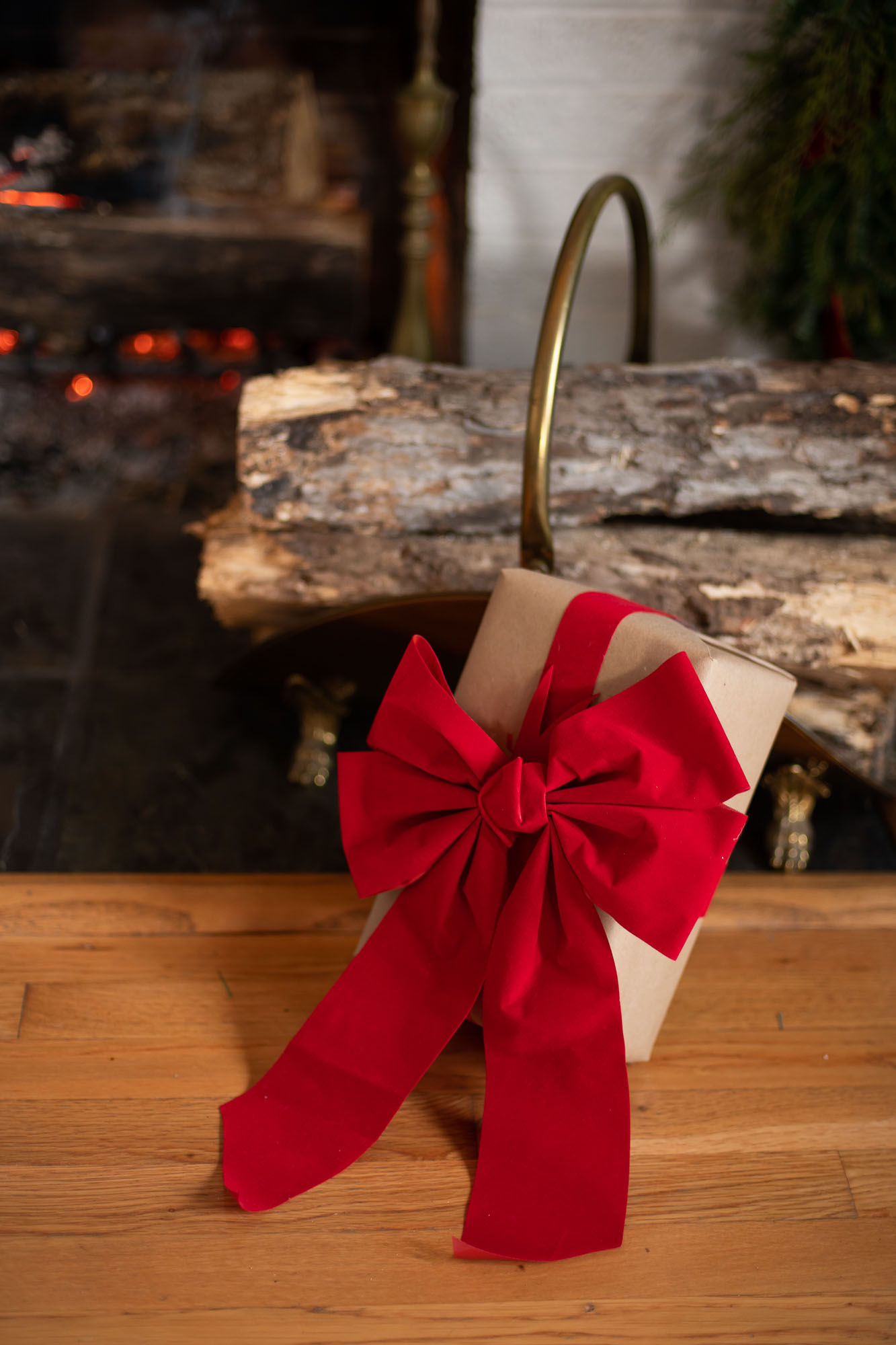 a christmas gift is resting in front of a roaring fire wrapped in brown paper and tied up with red velvet ribbon and a large red bow