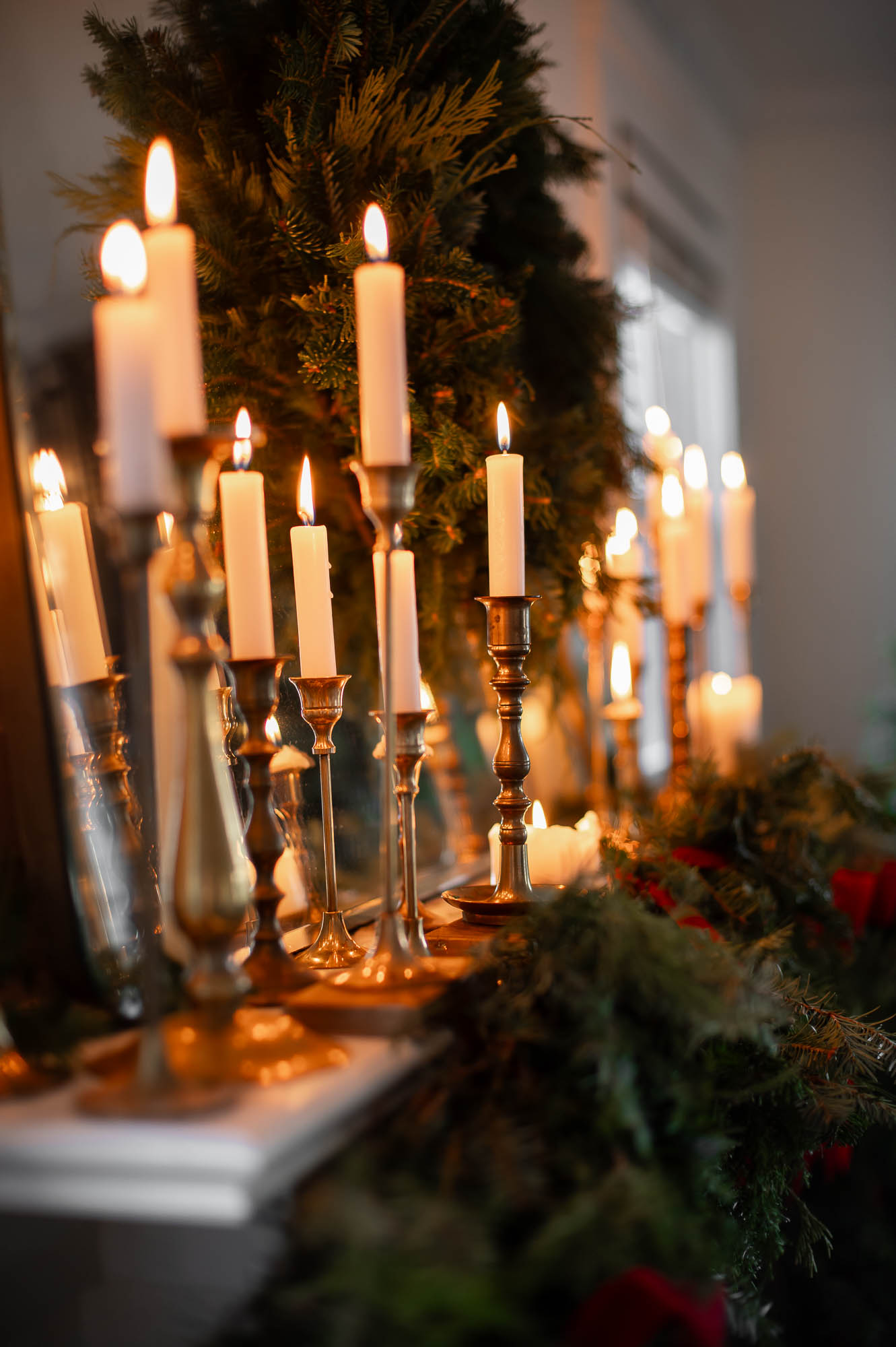dozens of lit candles in vintage brass candlestick holders line a old world christmas mantle