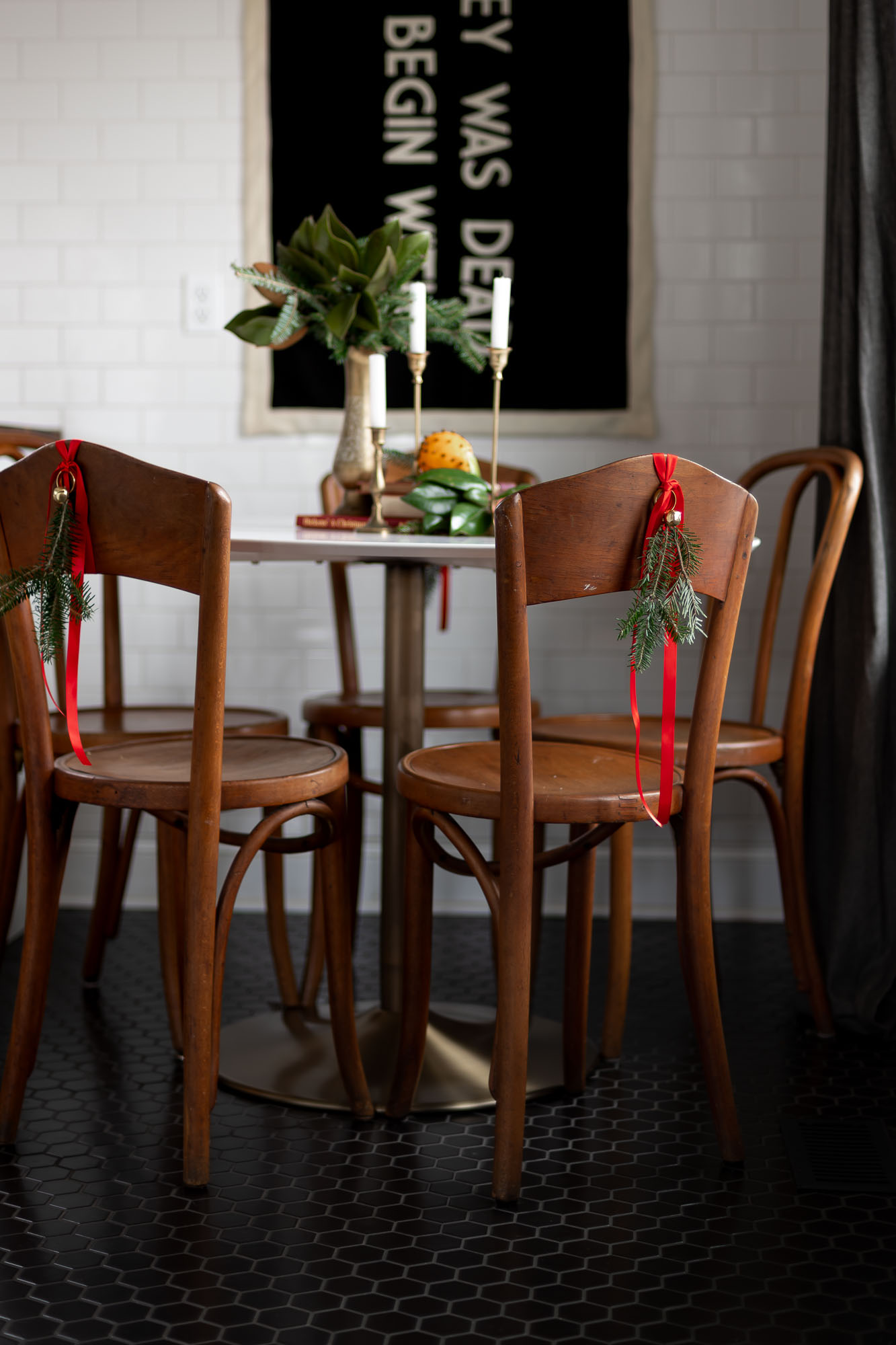 a sprig of fresh evergreen tied with a brass jingle bell hangs on the back of a set of vintage bentwood dining chairs in a small dining nook.