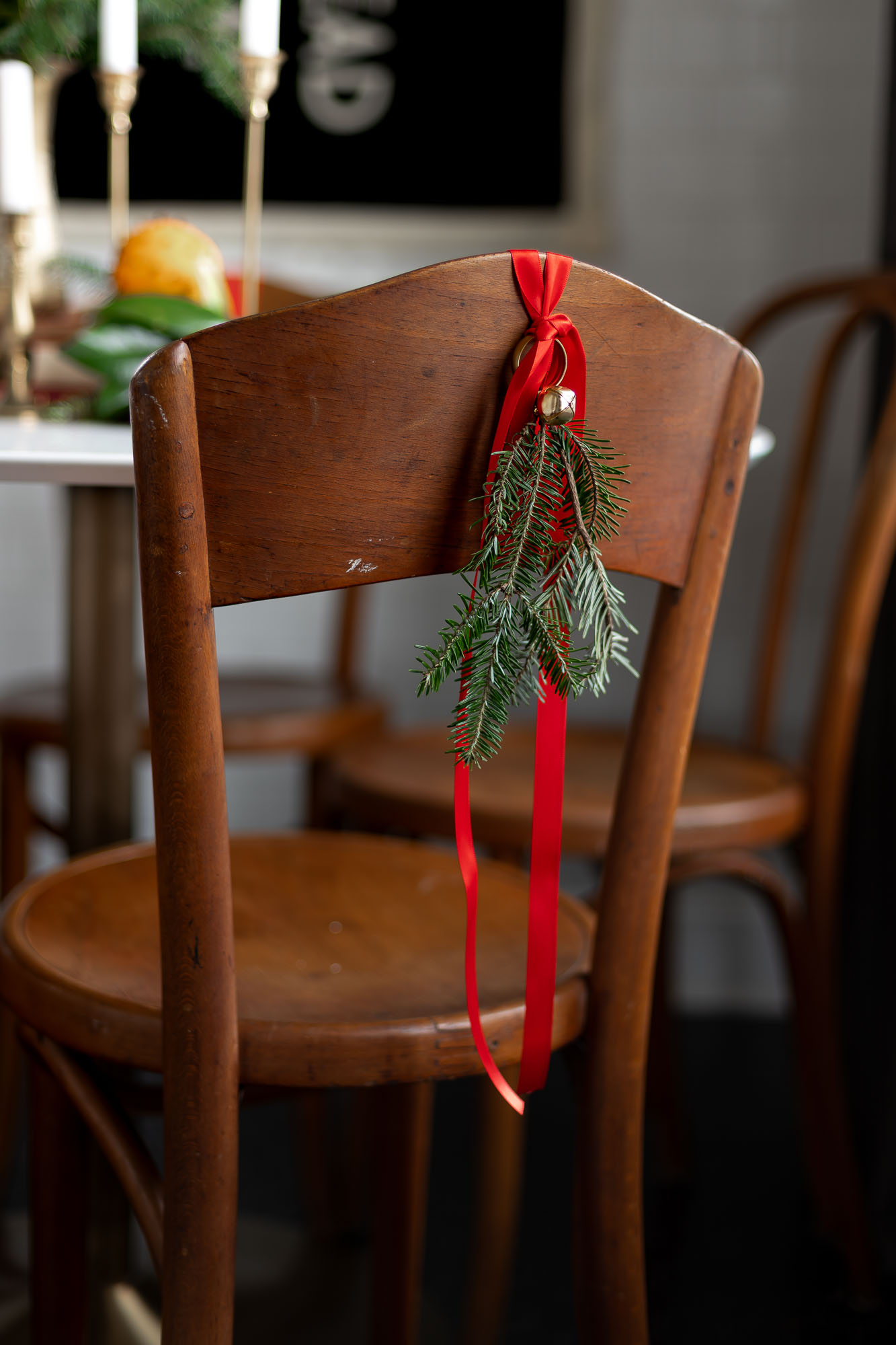 a sprig of fresh evergreen tied with a brass jingle bell hangs on the back of a set of vintage bentwood dining chairs in a small dining nook.