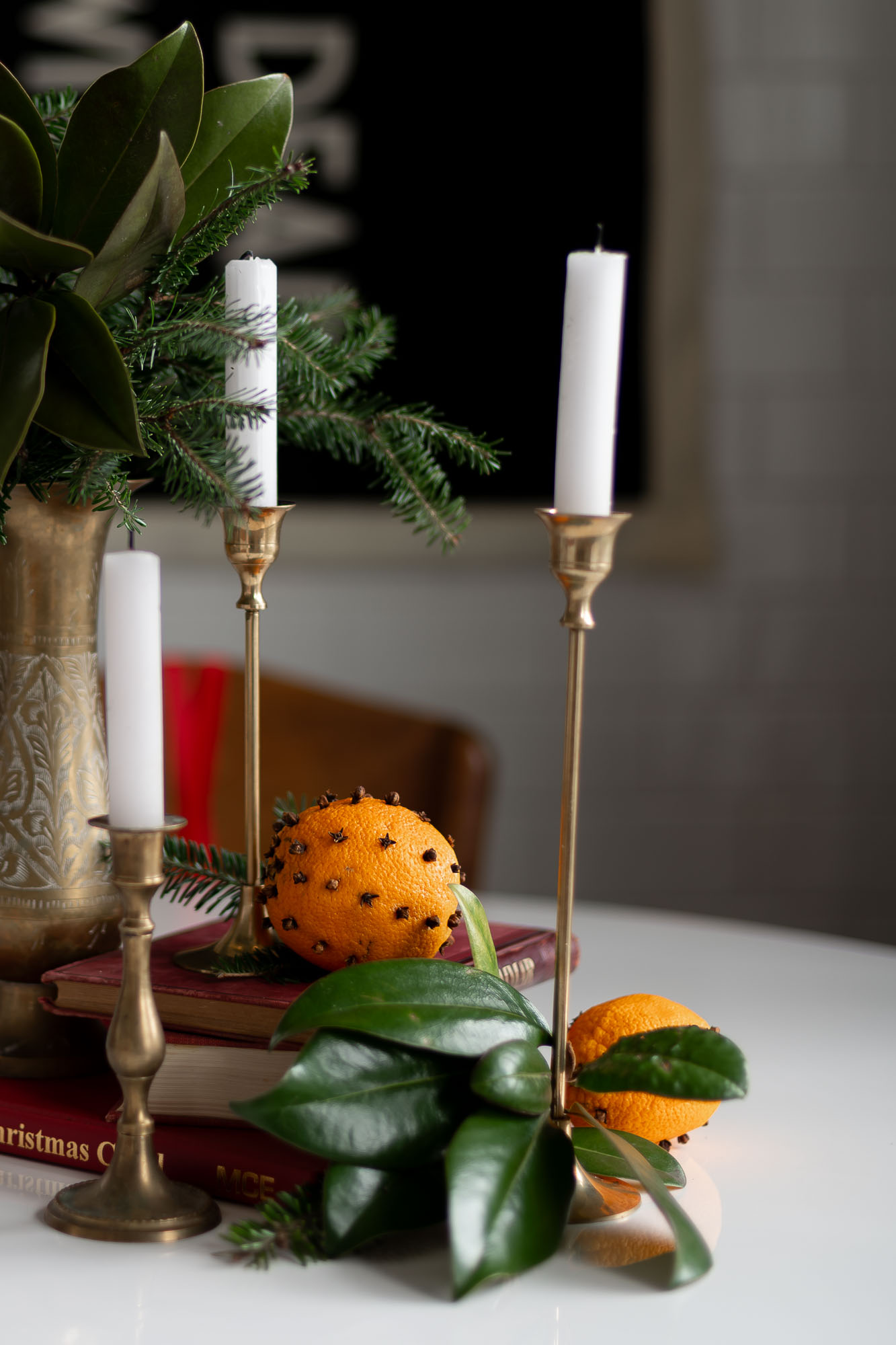 clove studded orange on a stack of old books with brass candlestick holders and evergreen branches