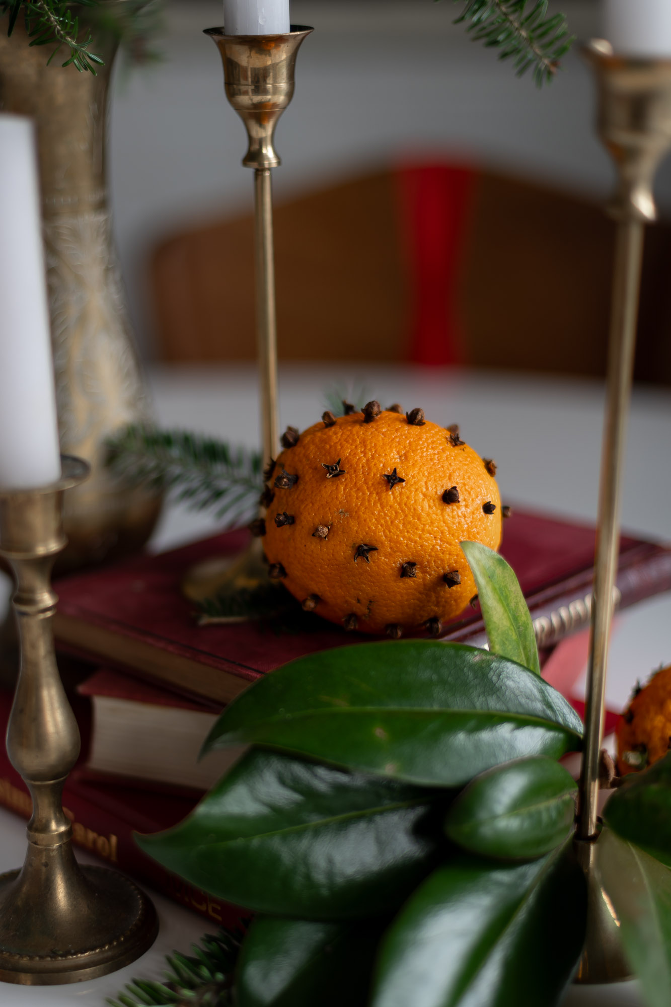clove studded orange on a stack of old books with brass candlestick holders and evergreen branches