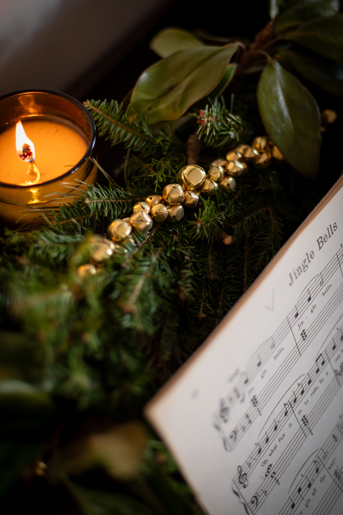 diy garland made from brass jingle bells is woven into fresh evergreen garland on top of a piano.