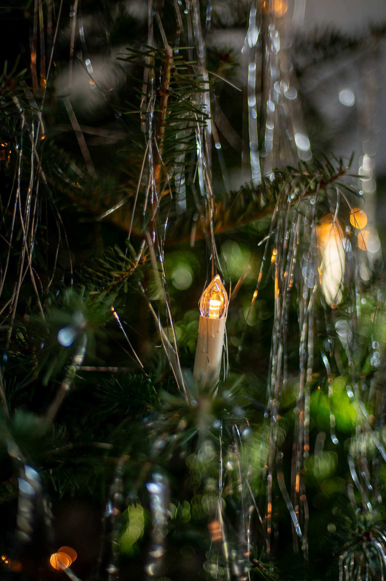 a led wired clip on candlestick christmas tree light rests on the branches of a christmas tree decorated with silver tinsel.