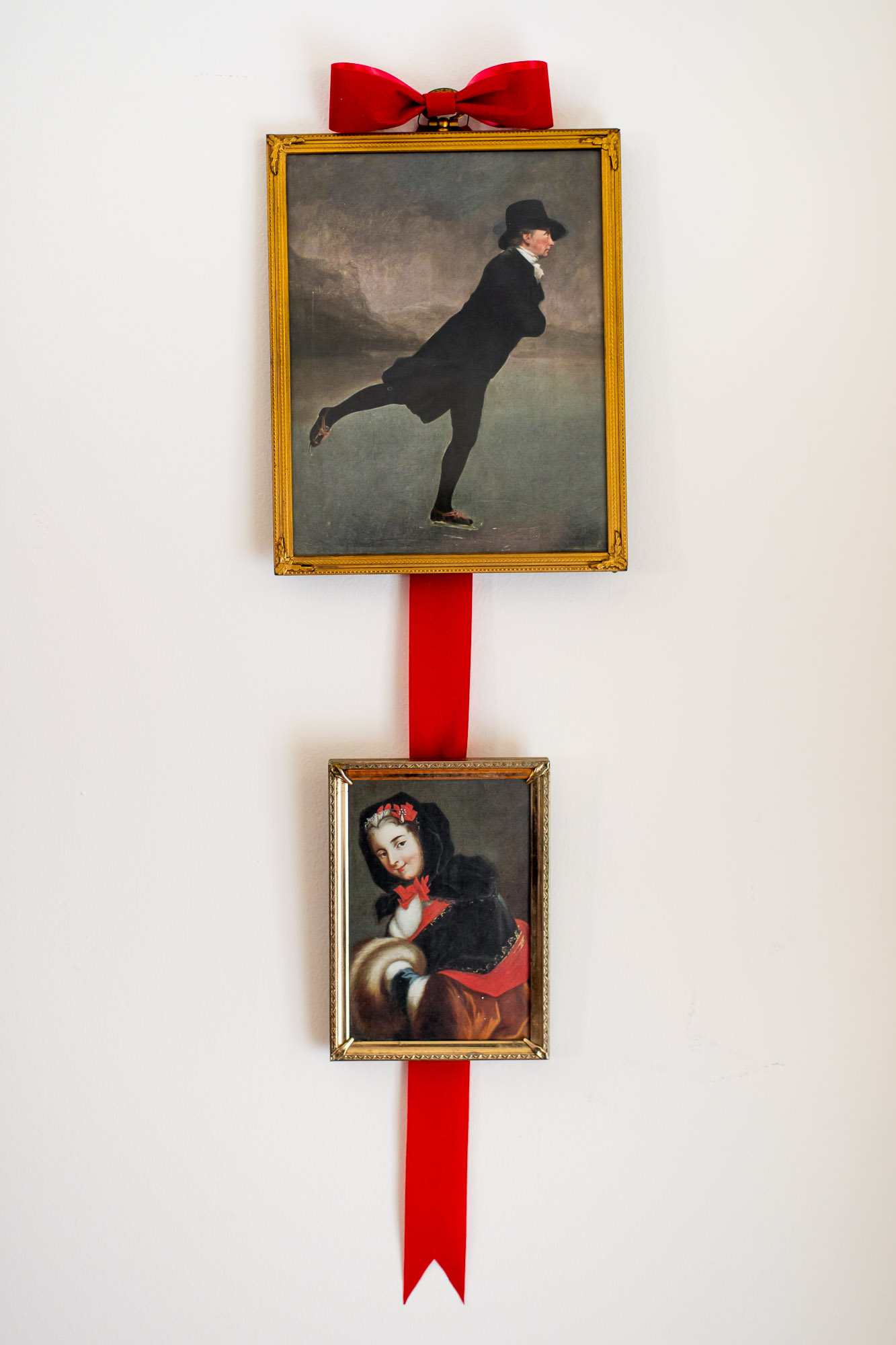 two brass picture frames filled with vintage christmas wall art hang from a red velvet ribbon