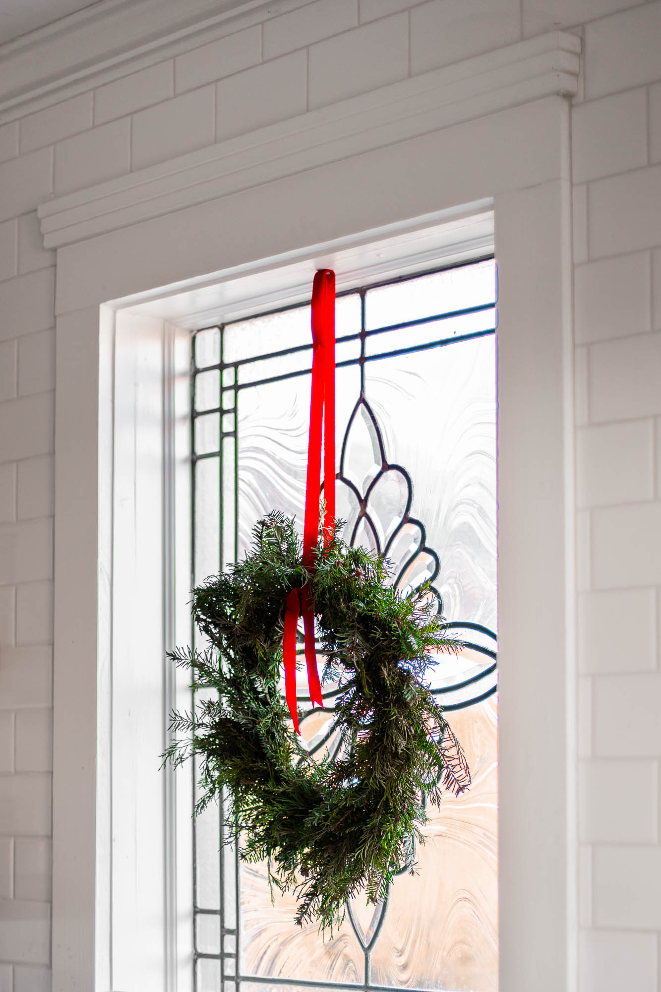 a simple fresh evergreen wreath hangs in a window in a vintage kitchen