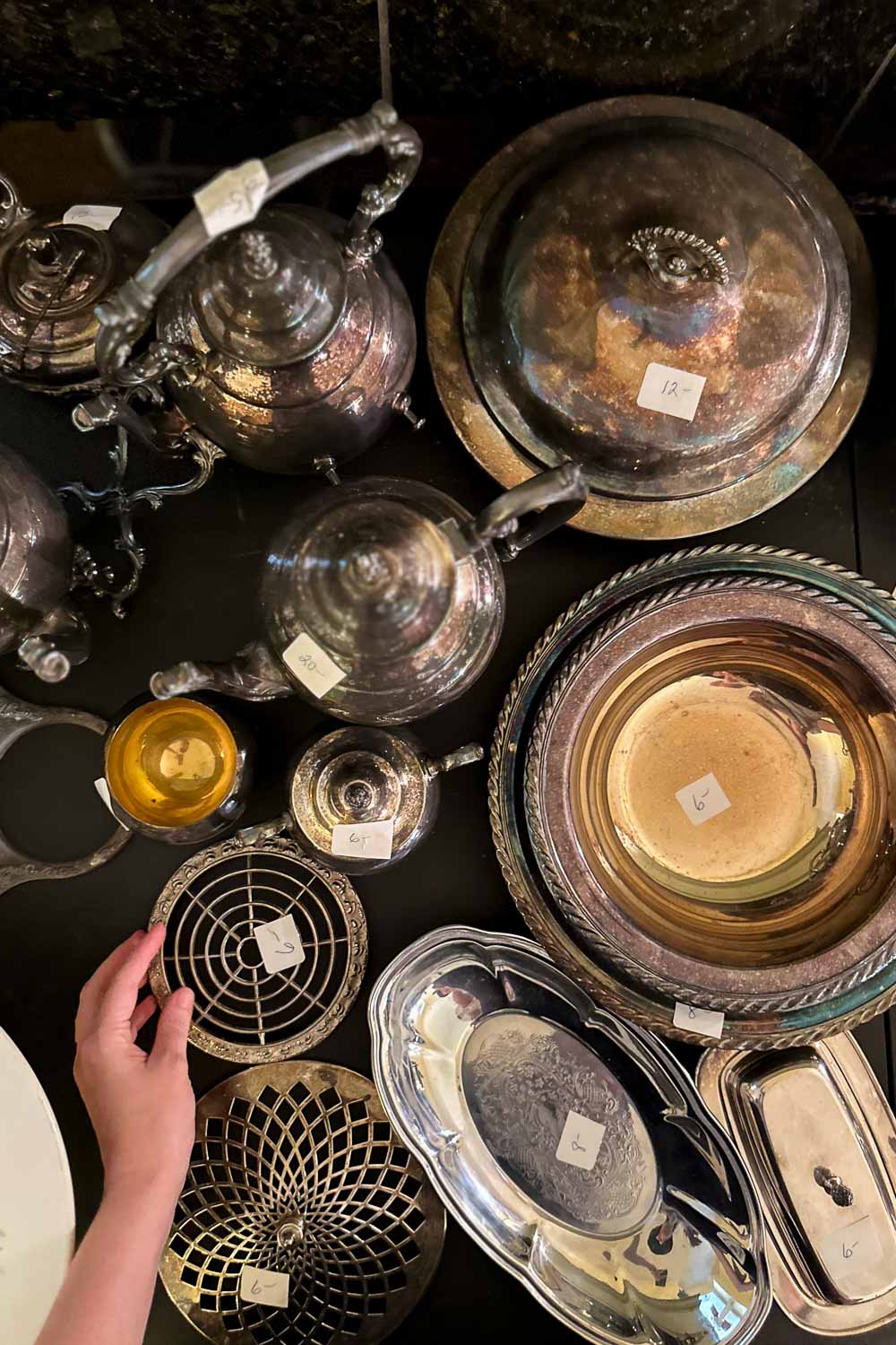 a collection of vintage silver serving ware on a table at an estate sale with handwritten price tags