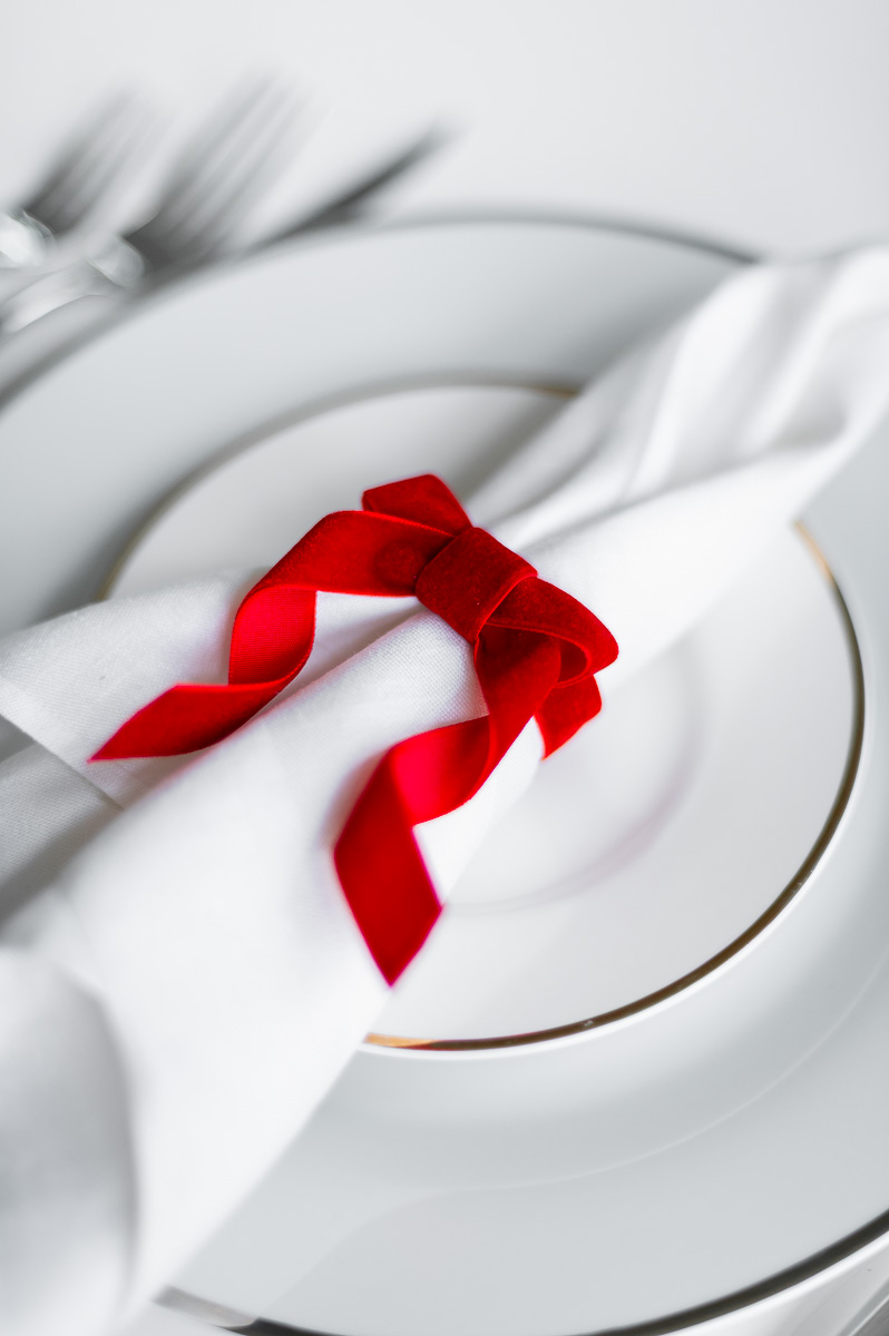 DIY red velvet napkin ring on a white linen napkin, styled for a Christmas holiday table setting as Christmas Napkin Rings