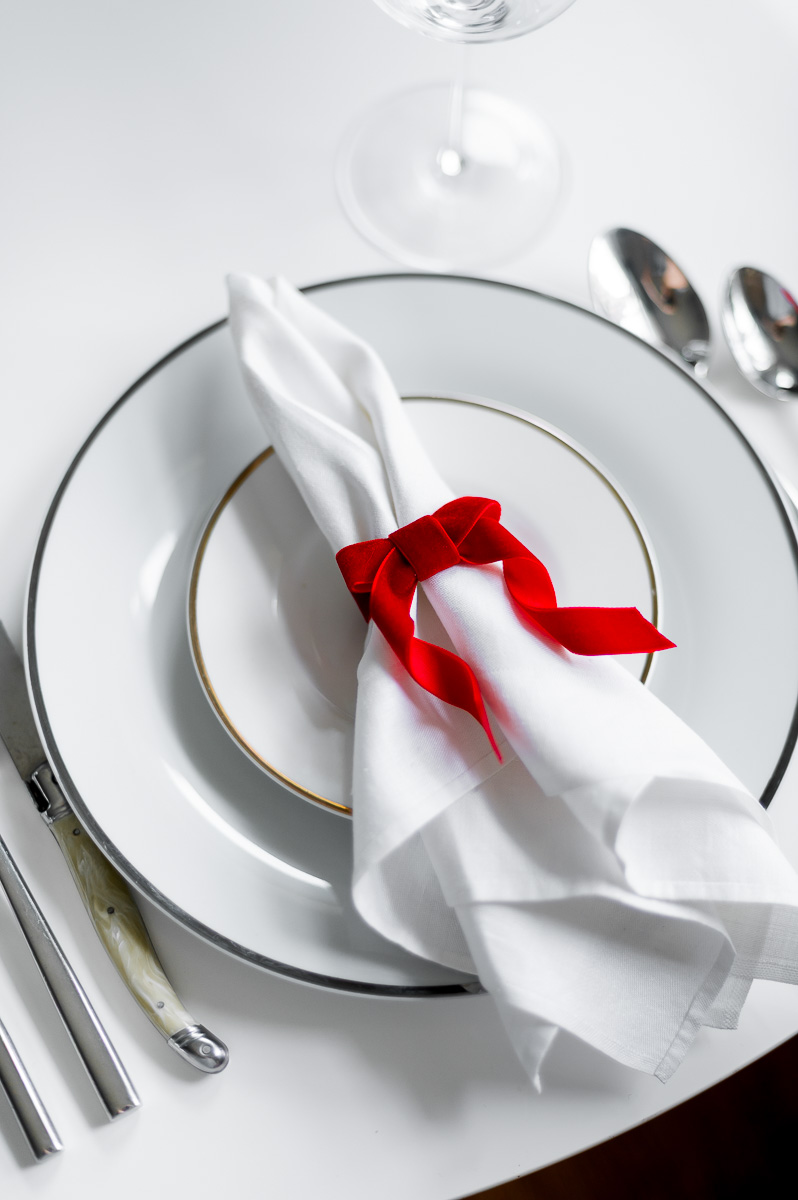 DIY red velvet napkin ring on a white linen napkin, styled for a Christmas holiday table setting as Christmas Napkin Rings