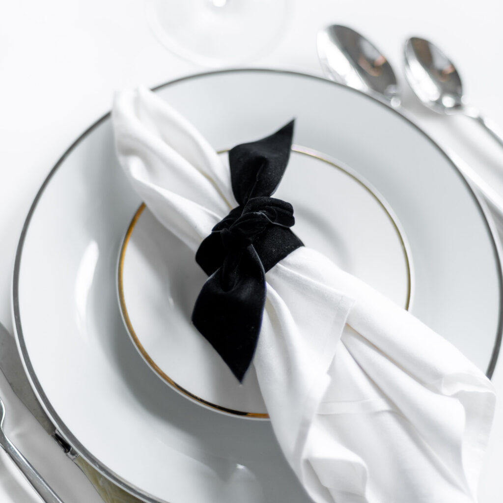 DIY Napkin Ring created from black velvet ribbon holding a white napkin laid on a formal place setting