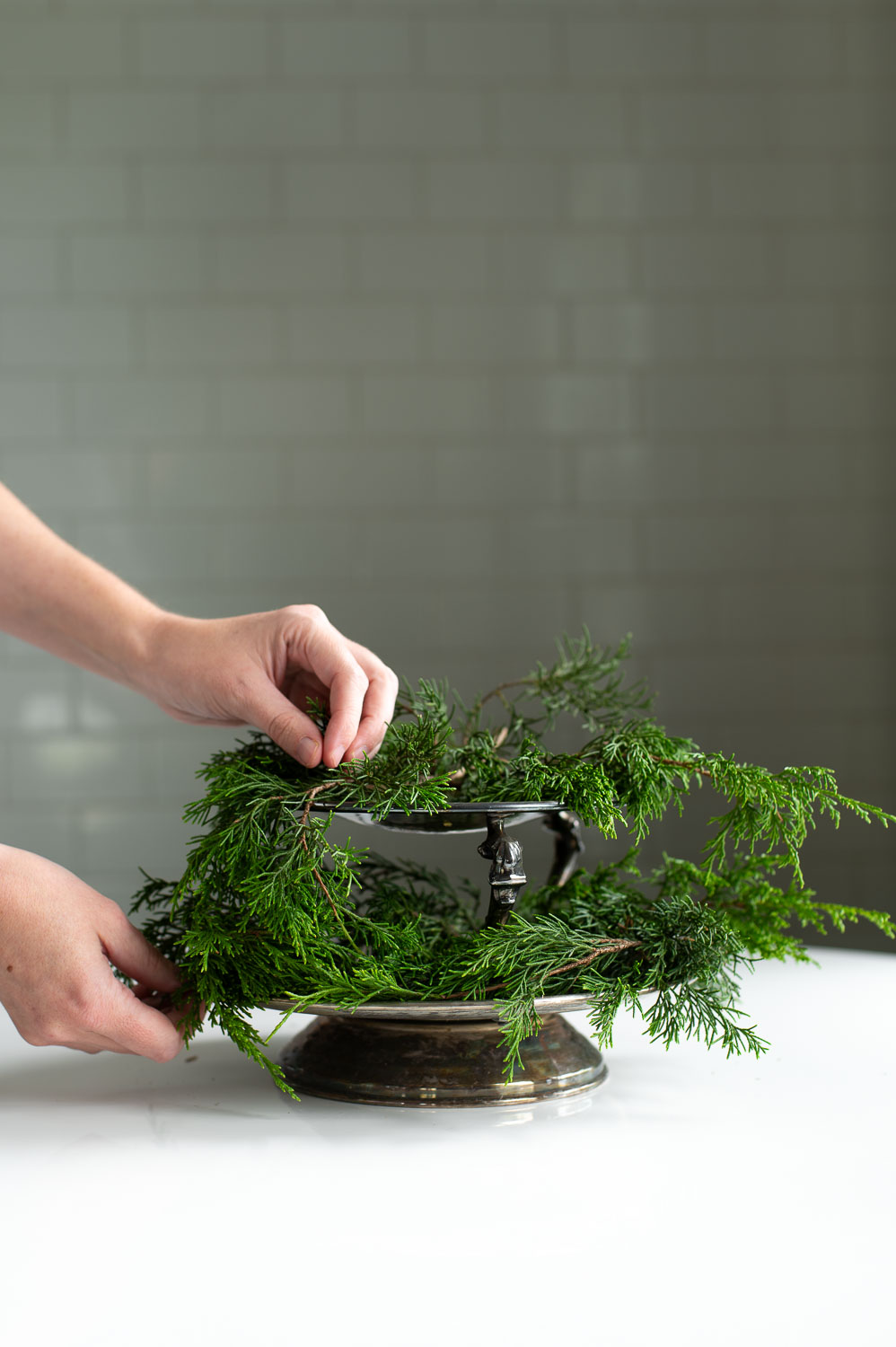 a woman places springs of Christmas greenery onto a thrifted two tier serving tray.