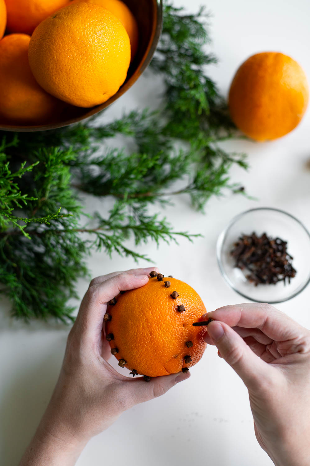 a woman holds an orange and places a whole clove into a poked hold to create a clove-studded orange pomander.