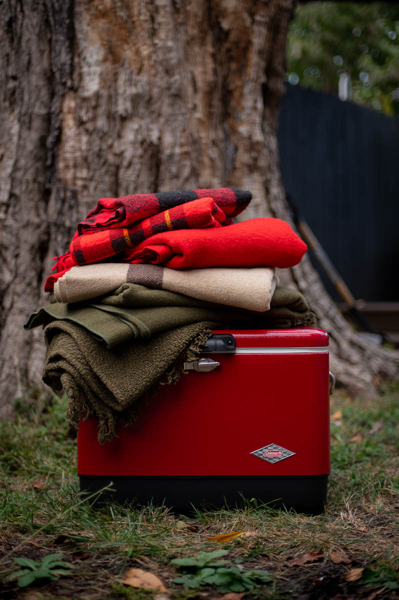 Cozy fire pit party decor with vintage red Coleman cooler and plaid blankets – perfect for a fall bonfire night party.