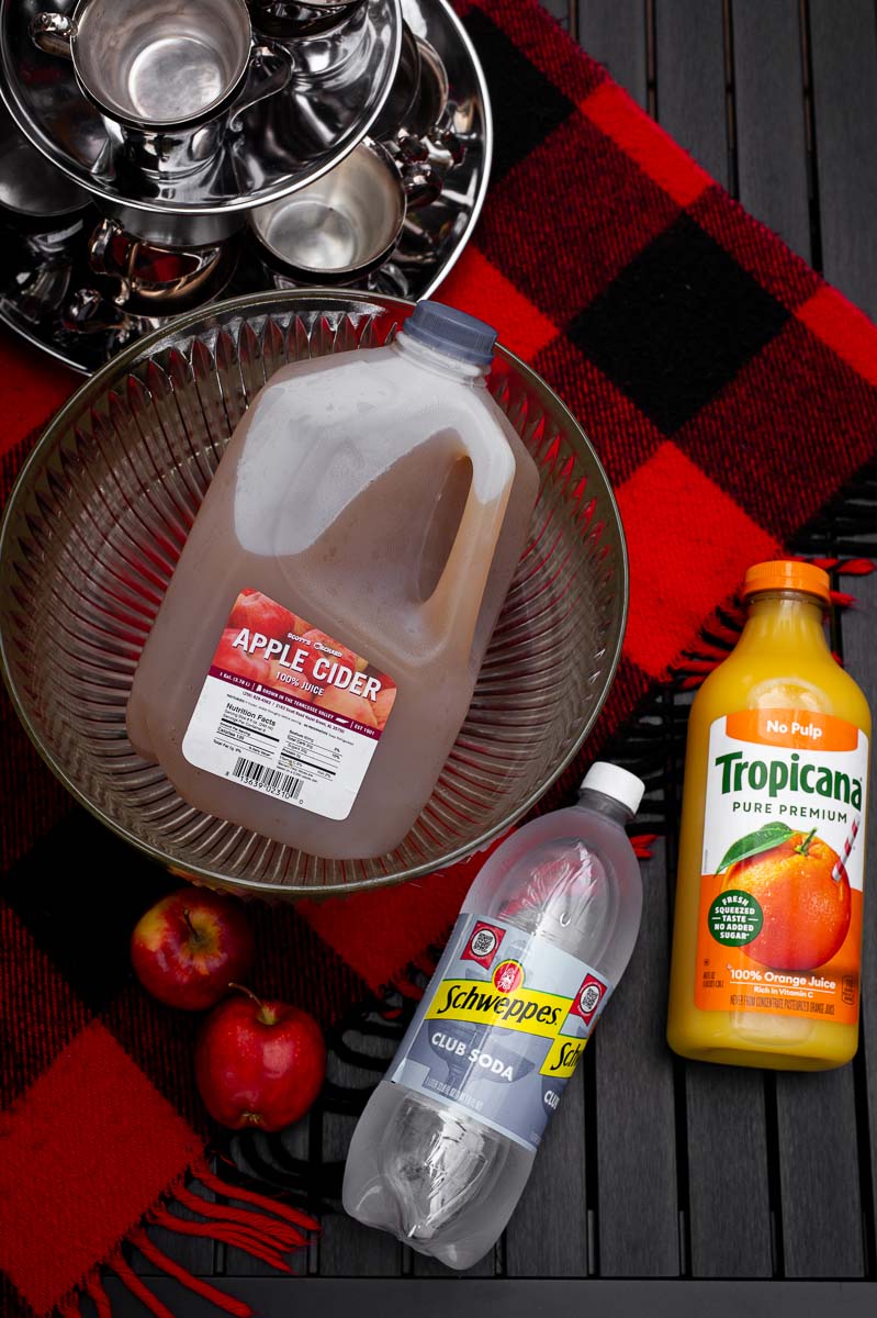 Flat lay of apple cider, orange juice, and sparkling water ingredients for apple cider punch non alcoholic, perfect for fall punch recipes non alcoholic, harvest punch, and Thanksgiving punch non alcoholic.
