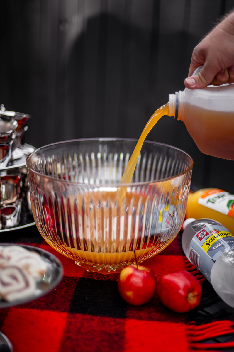 Apple cider being poured into a vintage glass punch bowl for apple cider punch non alcoholic, perfect for harvest punch, fall party punch, and autumn punch recipes non alcoholic.