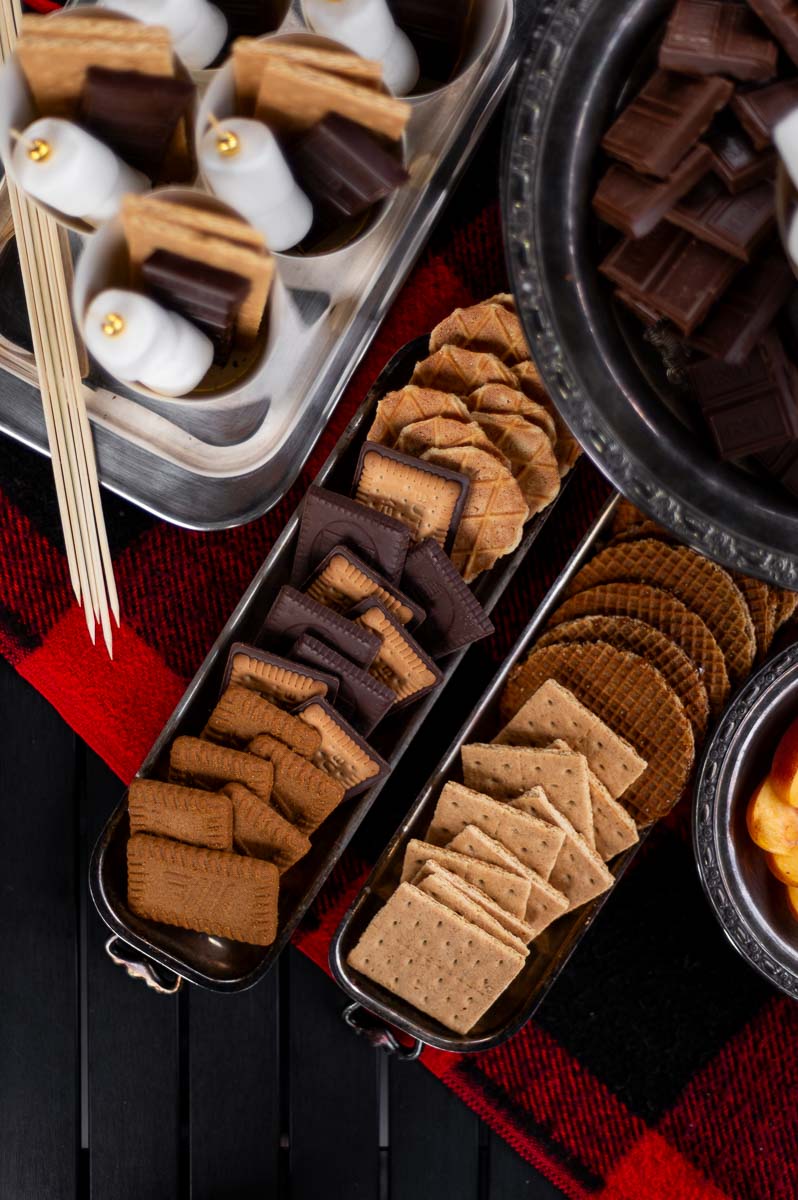 Close-up of graham crackers, marshmallows, and fresh fruit – easy s’mores bar ingredients in silver dishes.