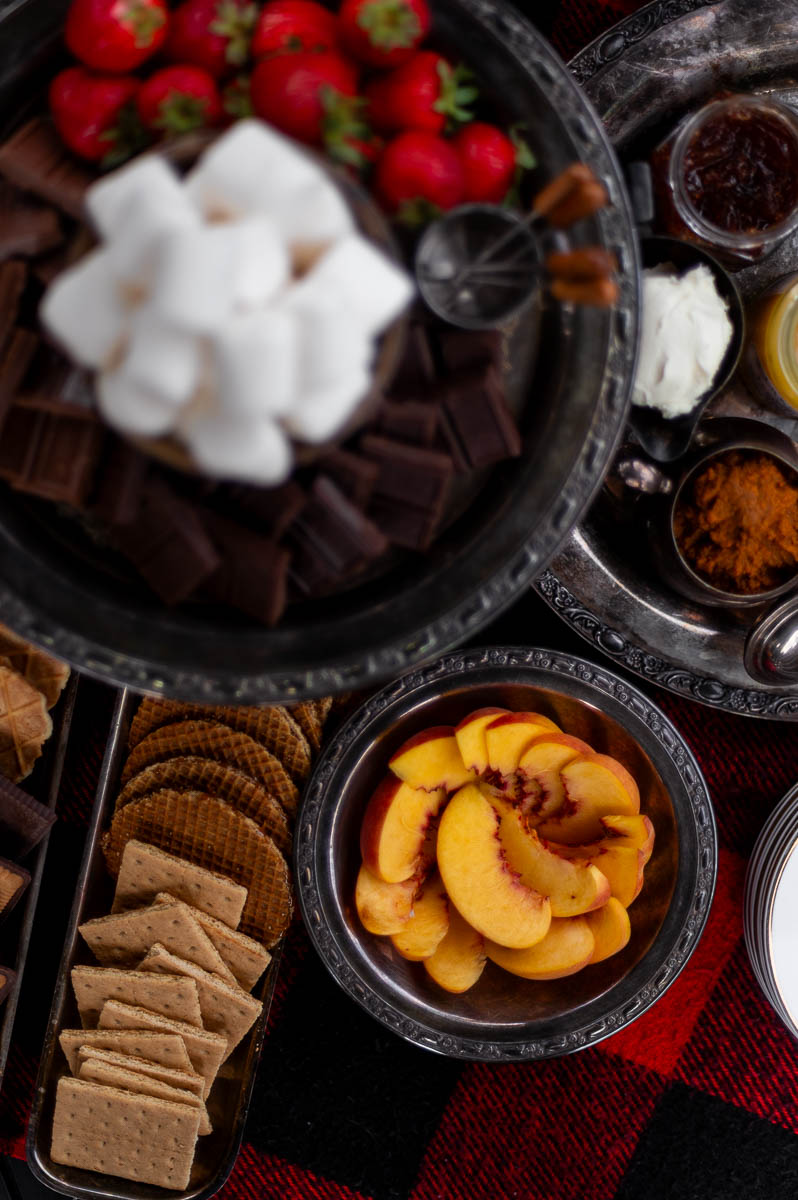 Close-up of graham crackers, marshmallows, and fresh fruit – easy s’mores bar ingredients in silver dishes.