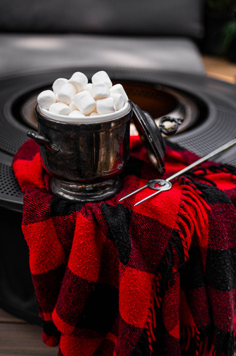 Backyard bonfire party setup with vintage plaid blankets and silver servingware – fall bonfire party ideas.