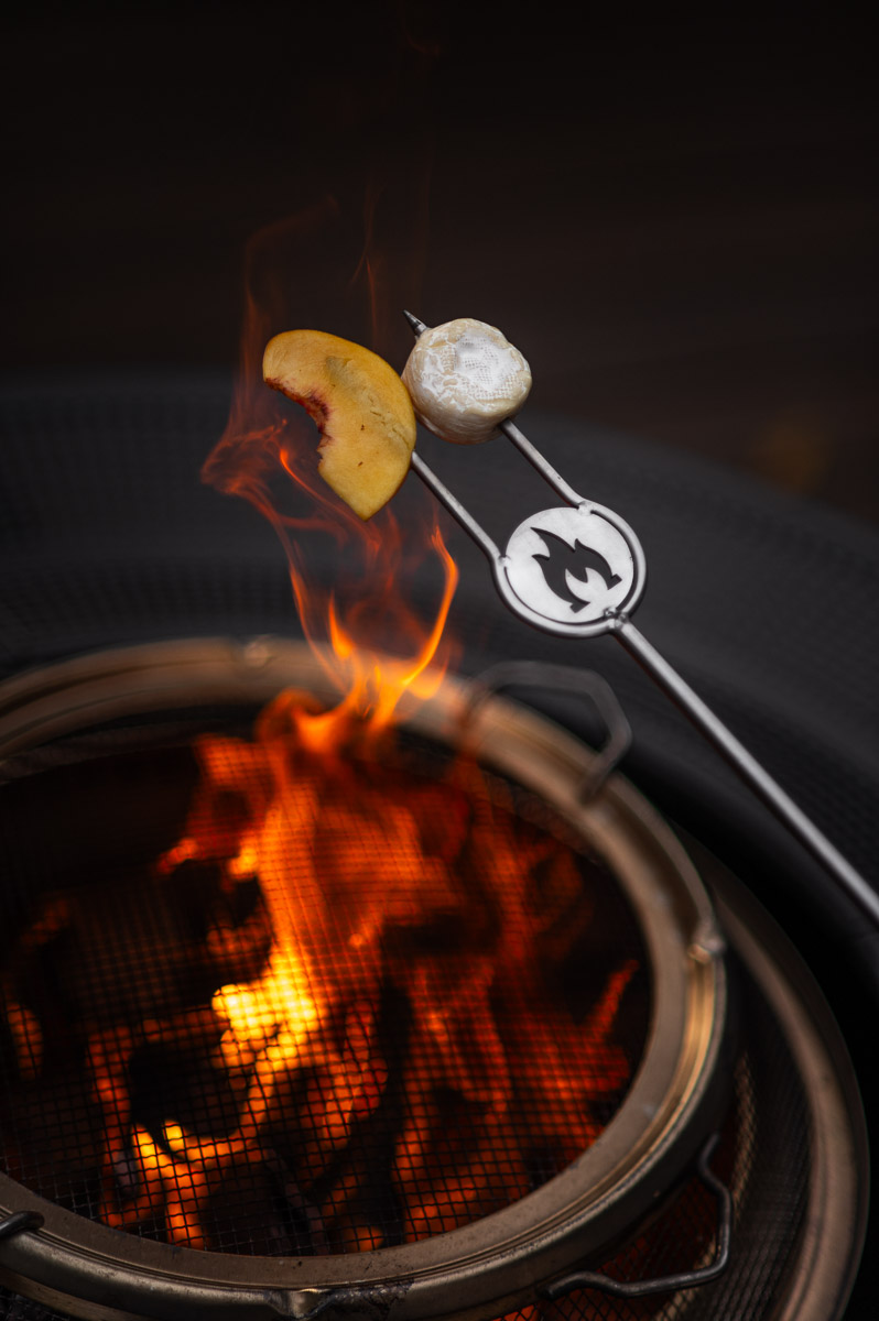 Guests roasting savory s'mores with peaches and brie over a campfire at a backyard bonfire party.