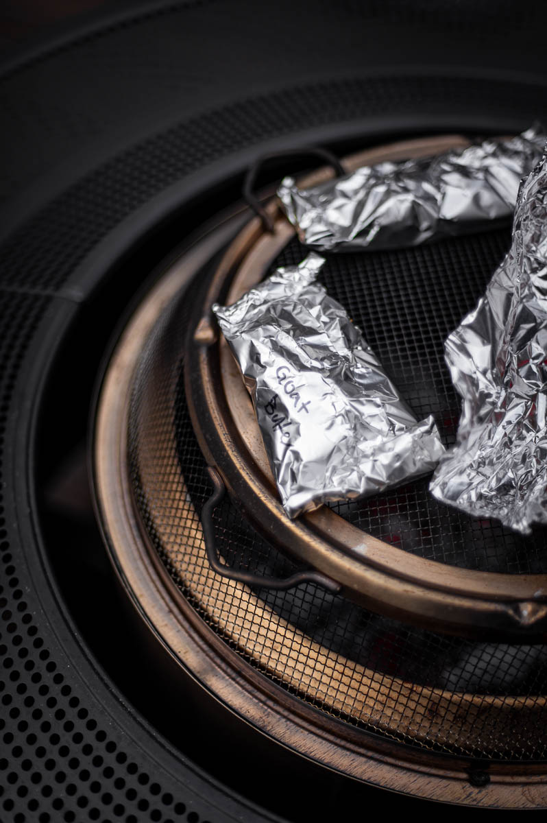 Foil packets roasting over a Solo Stove fire pit at a backyard bonfire party, filled with apples, butter, and goat cheese.
