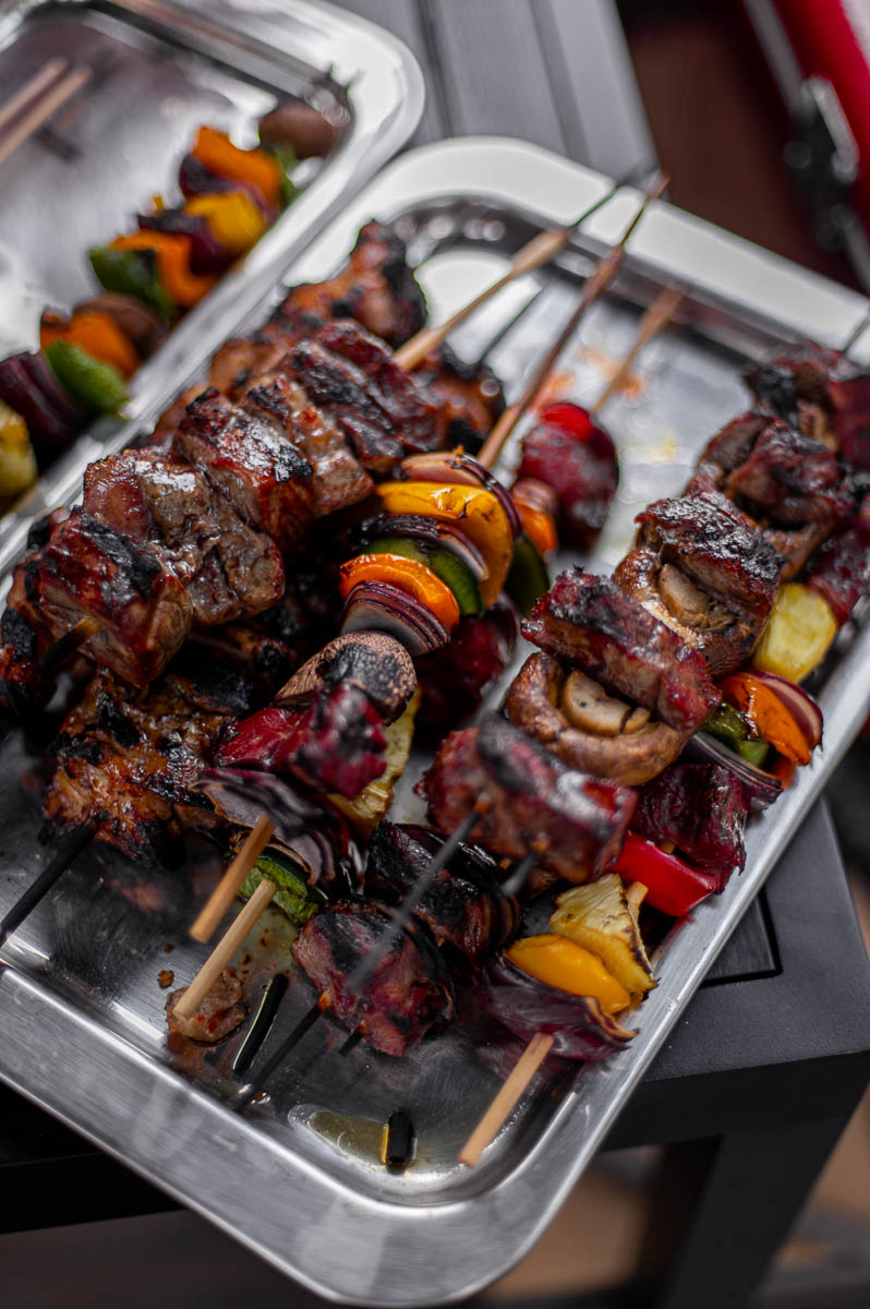 Beef, chicken, and veggie kabobs arranged on a silver tray for a backyard bonfire party food.
