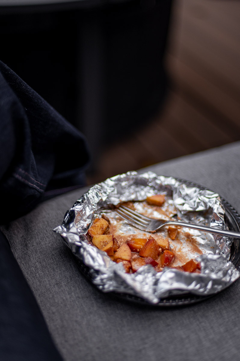 Opened foil packets with roasted apples, butter, and goat cheese served on a silver plate for a fall bonfire party appetizer.