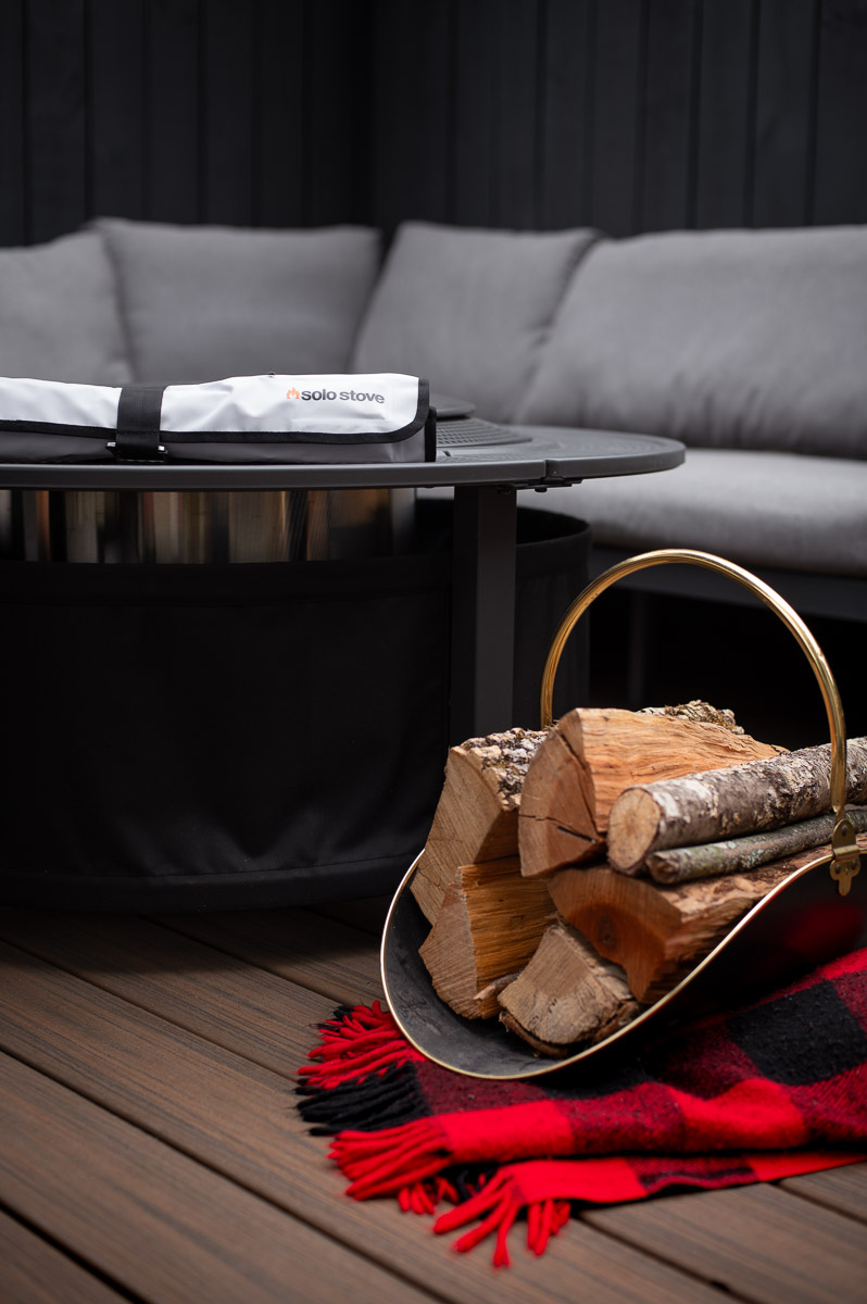 solo stove fire roasting sticks shown bundled up in their carry case resting on top of the solo stove surround next to a rack of firewood on a deck.
