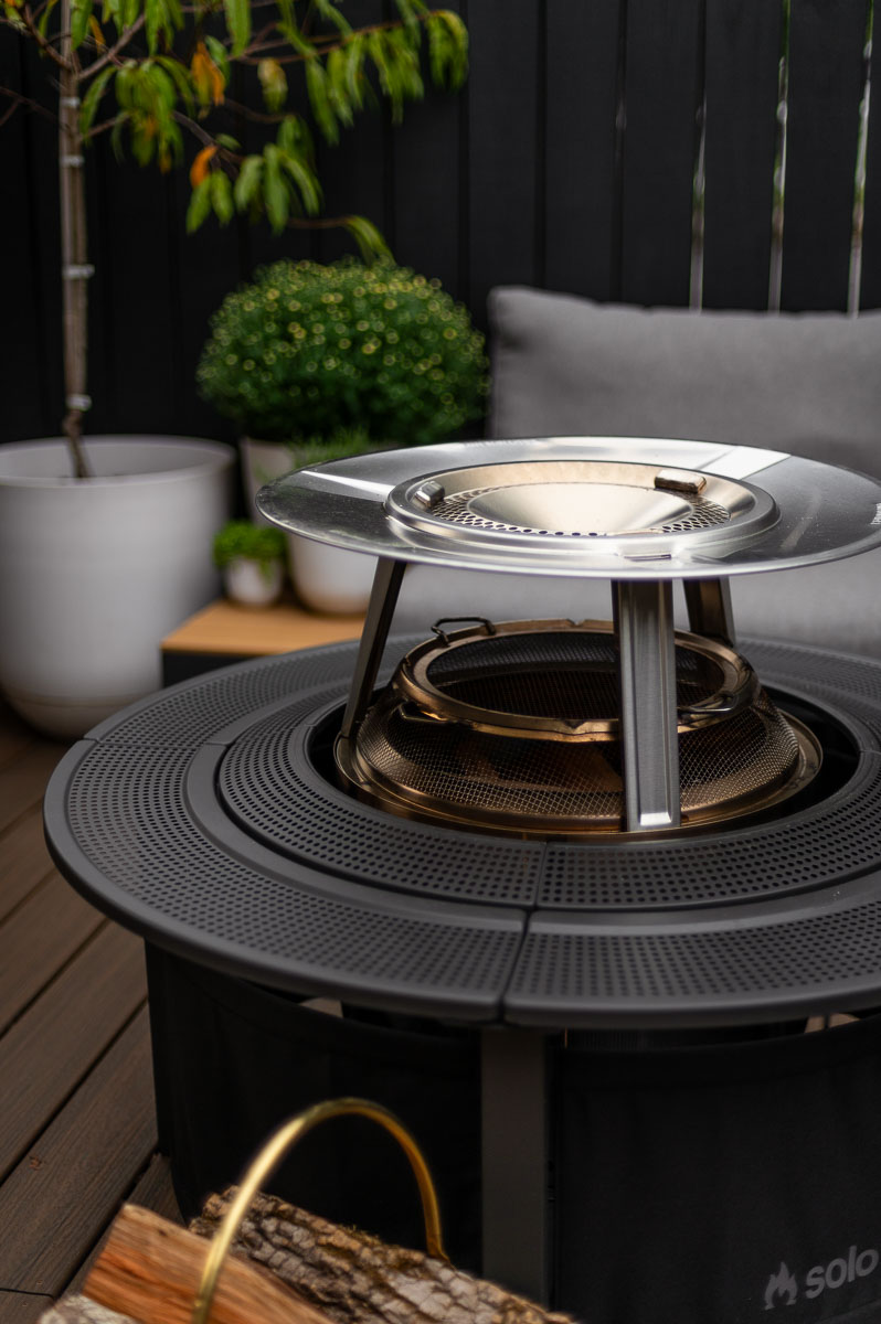 close up of solo stove accessories displayed on a bonfire fire pit showcasing the solo stove heat deflector, solo stove shield and solo stove surround set-up on a deck. 
