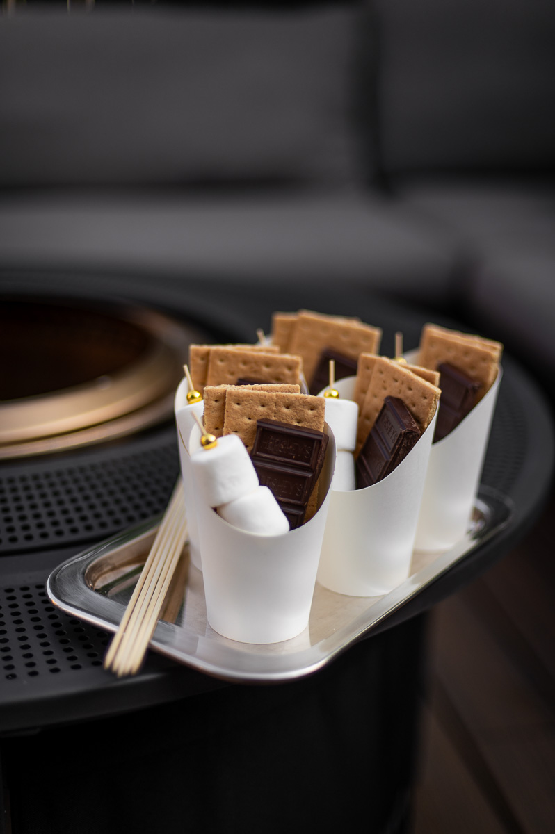 DIY S'mores kits filled with marshmallow skewers, chocolate bars and graham crackers sit on a silver tray on a solo stove ready to serve at a fire pit party.