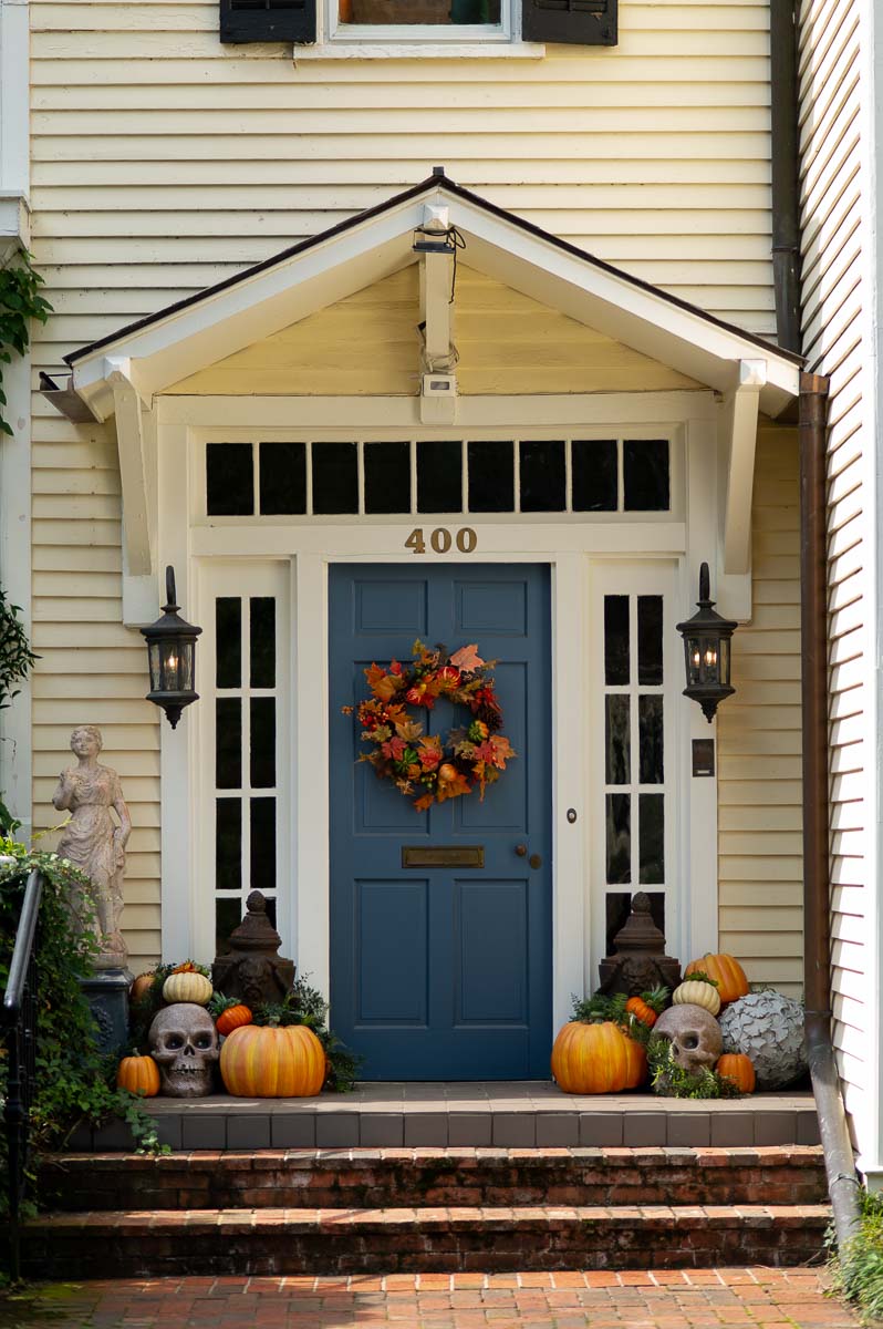 fall porch decor with pumpkins, large concrete skulls, ivy and a fall front door wreath made with fall leaves