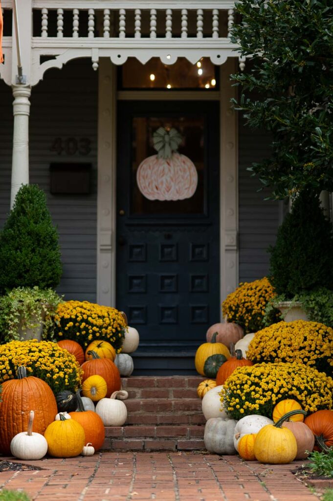 mum fall front porch display with yellow mums and orange, yellow and white pumpkins in front of a historic home.