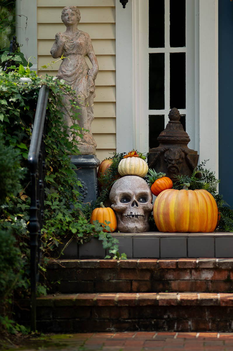 fall porch decor with pumpkins and a large concrete skull covered in ivy.