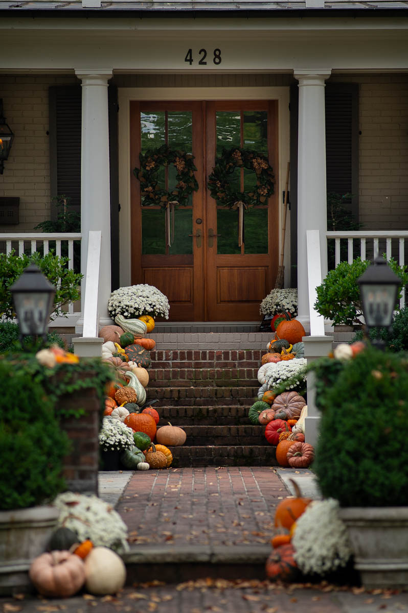 An example of southern fall porch decor featuring a collection of colorful fall pumpkins on stairs along with mums and gourds in a colorful exterior fall decor display in front of a historic home in Huntsville Alabama.