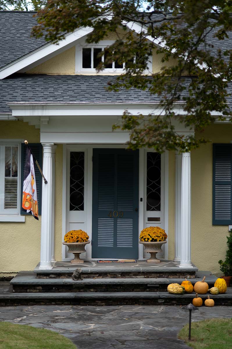 fall urns for front porch filled with yellow mums with a variety of pumpkins in front of a yellow house with a blue door