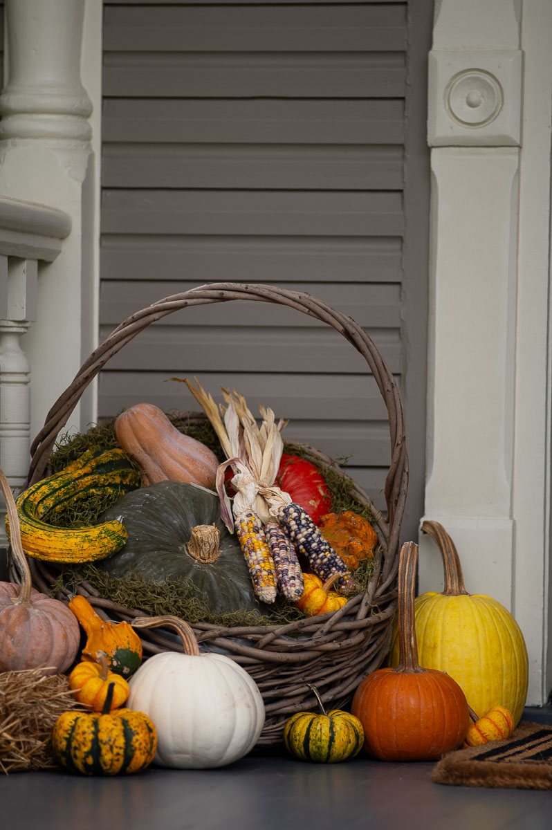 Elegant autumn front porch decor on a historic southern home featuring a harvest woven basket filled with pumpkins, gourds, corn, squash moss and hay for fall decor