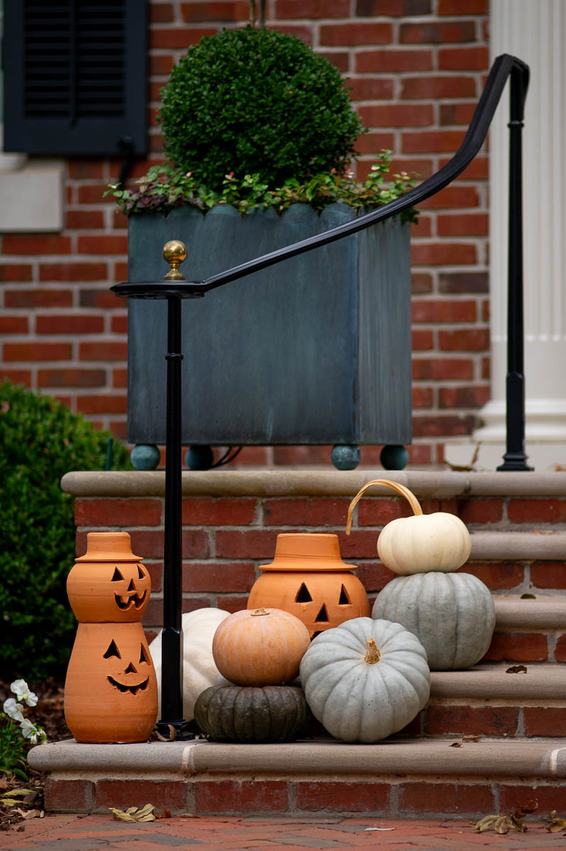 terracotta jack o lanterns and terracotta pumpkin lanterns sitting next muted fall pumpkins in a fall front porch display.
