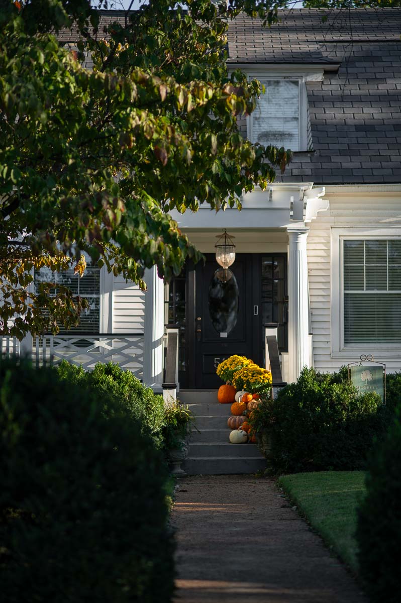 A cascade of fall pumpkins and mums spill down the front steps of a historic southern home as fall front porch decor