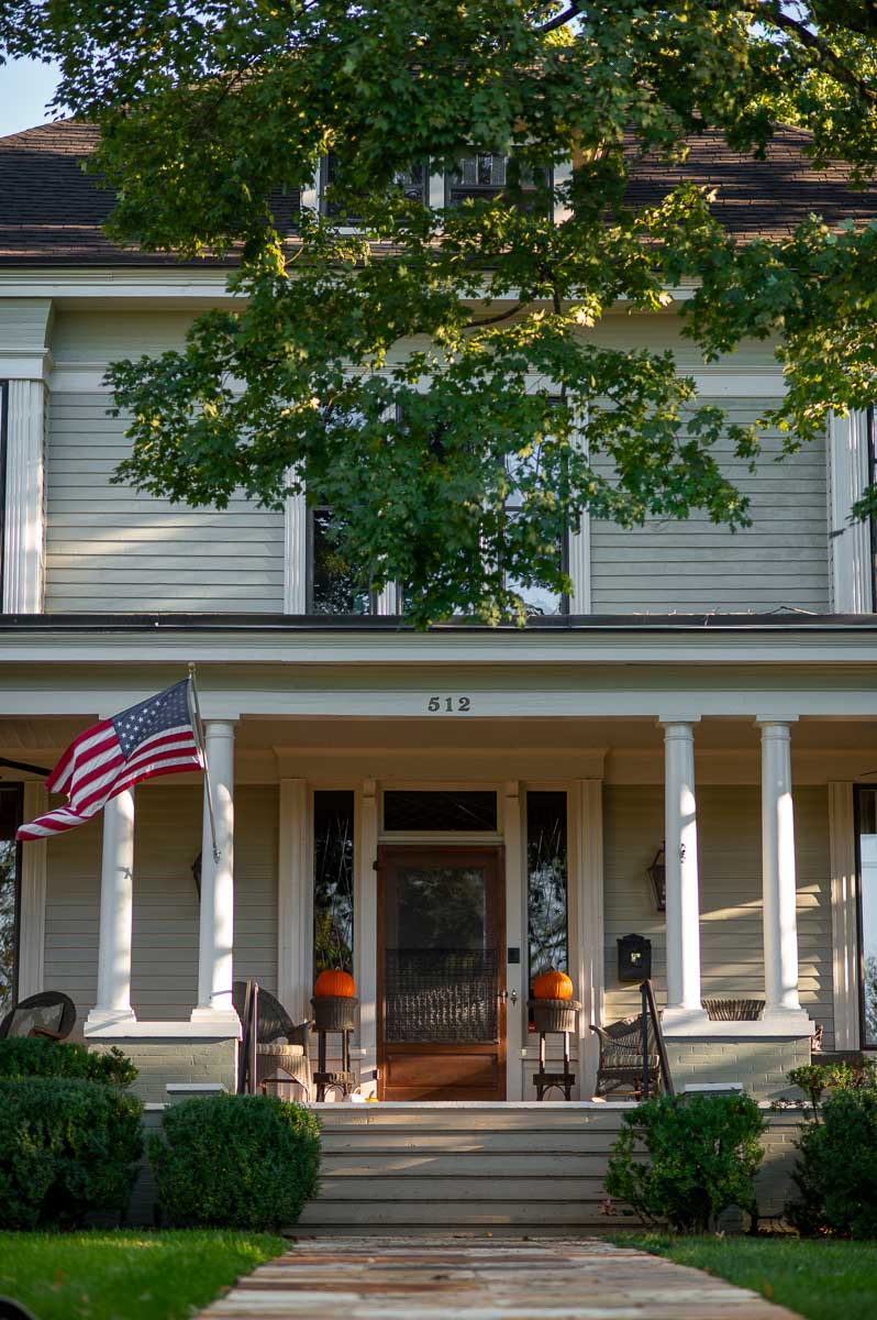 easy fall front porch decor using two pumpkins resting on wicker pedestals to either side of a front door on a historic home in Huntsville Alabama.