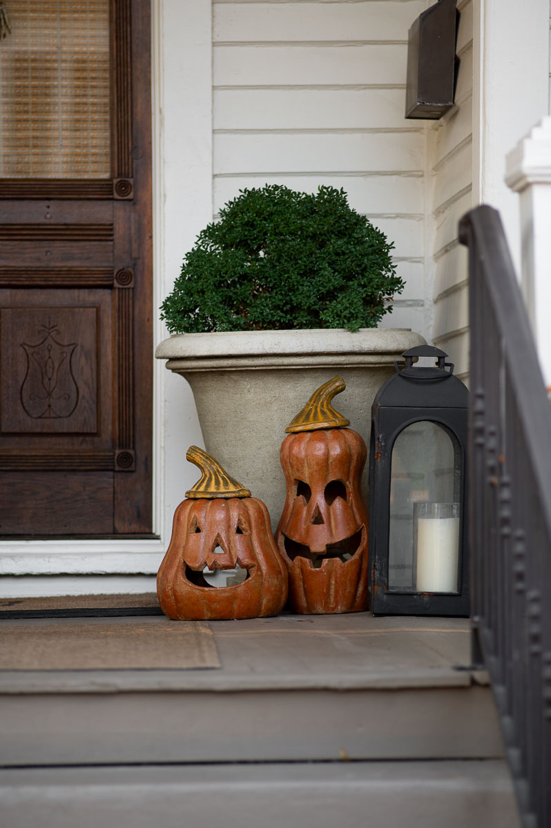 metal lanterns sit next to ceramic pumpkins as fall front porch decor in front of a white historic home in Huntsville Alabama.