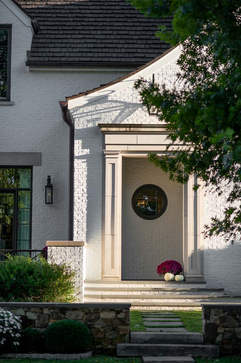 white pumpkins and a pink fall mum sit in front of a modern white brick home as modern fall porch decor.