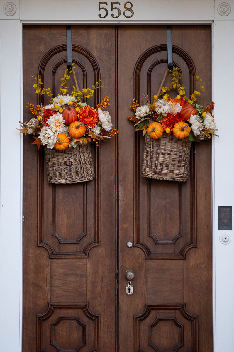 fall porch decorating ideas front doors showing a set of wood double doors with woven hanging baskets filled with pumpkins and flowers