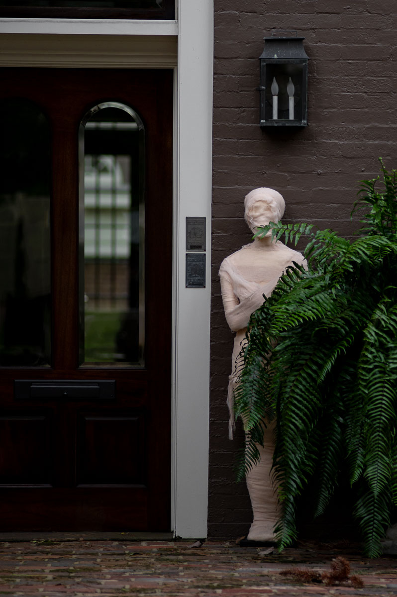 gauze wrapped mummy next to a giant fern in front of historic house to create elegant spooky Halloween front porch decor
