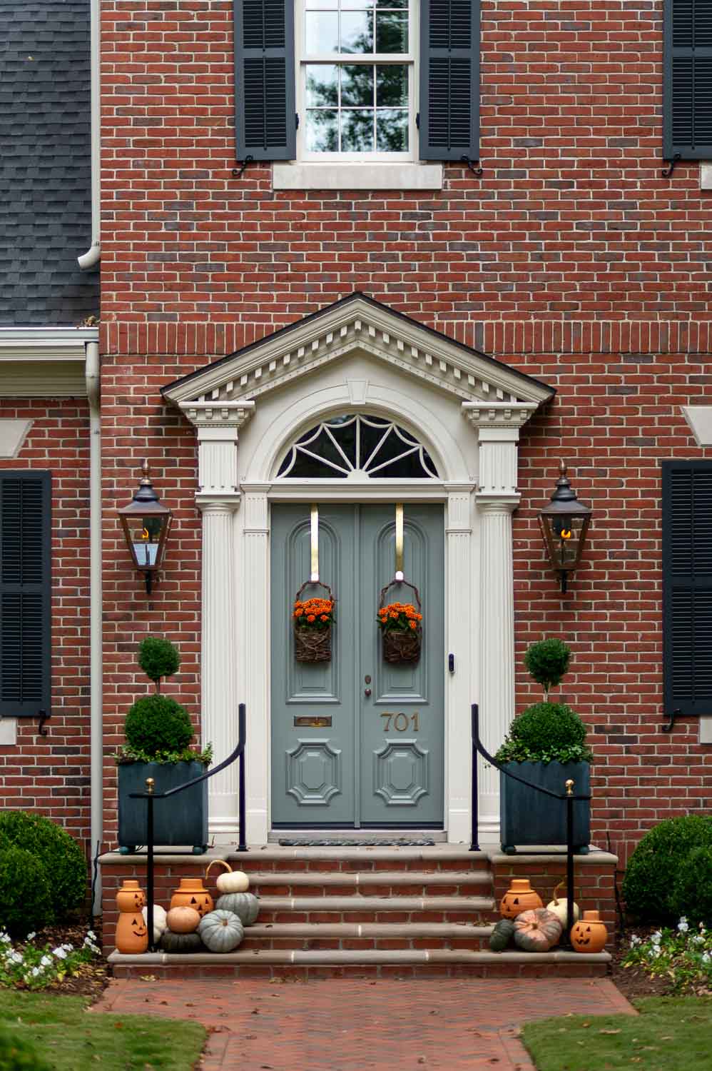 Historic southern fall porch decor with wicker hanging baskets filled with orange flowers, topiaries and terracotta pumpkins in Huntsville Alabama.