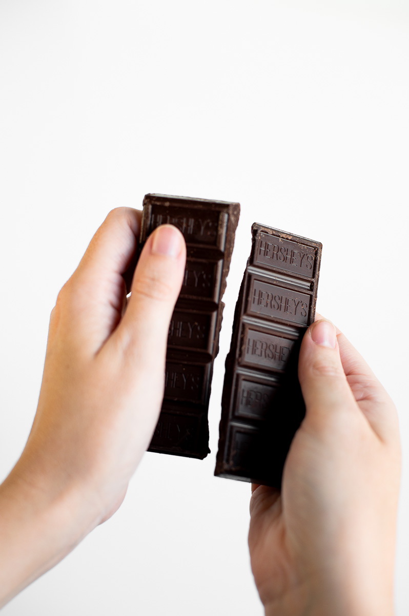 Chocolate bar being broken into strips to fill individual s’mores cups for an easy summer party dessert.