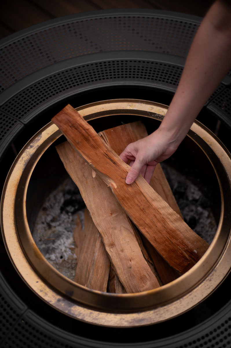 a woman places firewood into a solo stove on a deck for a fire pit party