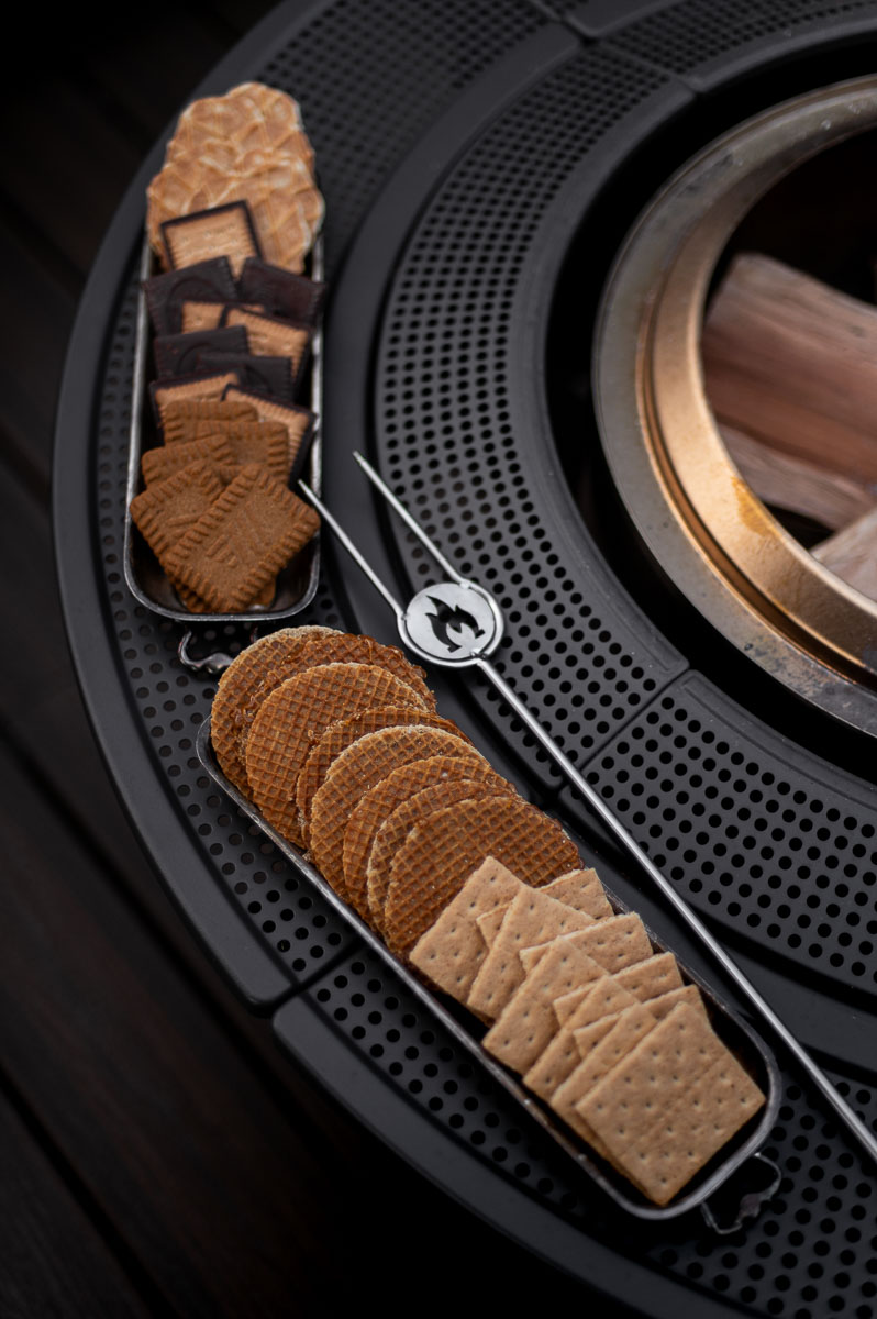 two vintage trays filled with s'mores ingredients for a bonfire party rest on the top of the solo stove surround next to the bonfire fire pit and a solo stove roasting stick