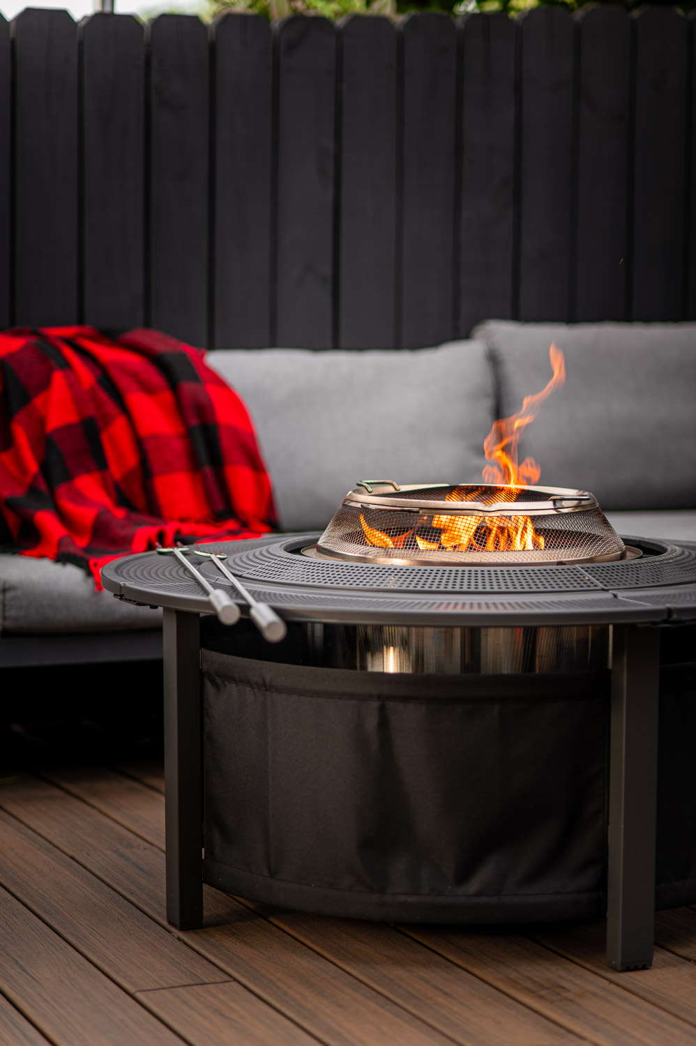 Solo Stove Bonfire burning on backyard deck near seating area with surround, spark shield and roasting sticks