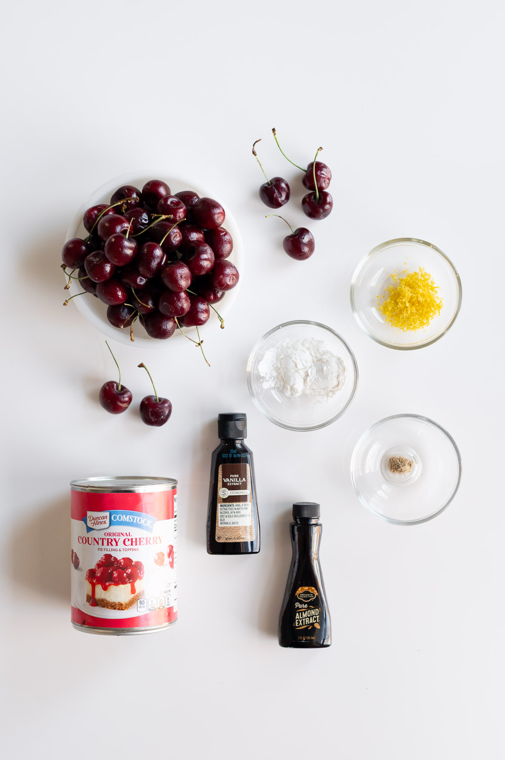 a collection of ingredients needed to bake semi-homemade cherry hand pies using upgraded canned filling rest on a table next to a bowl of fresh cherries