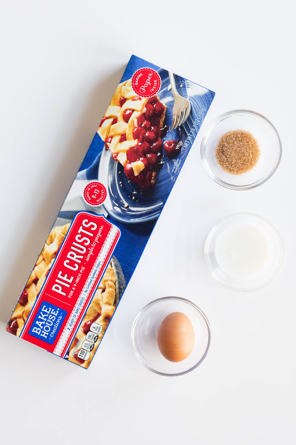 Store-bought ready made pie crust rest on a table next to an egg, some milk and coarse sugar in preparation for baking semi homemade cherry hand pies